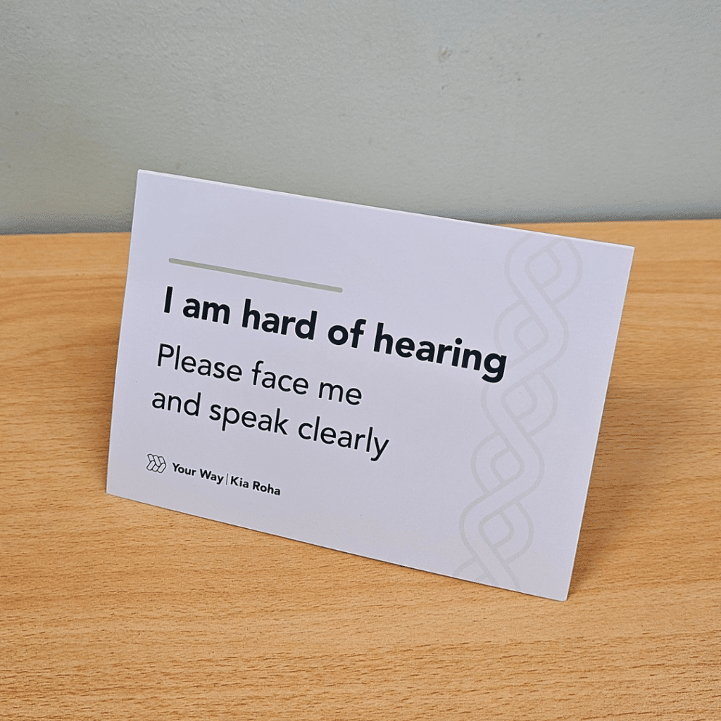 A bedside table card sits on a desk. It explains, 'I am hard of hearing. Please face me and speak clearly,"