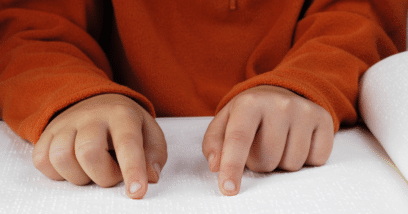 A person in an orange hoodie is reading a book written in braille, which is a common Alternate Format.