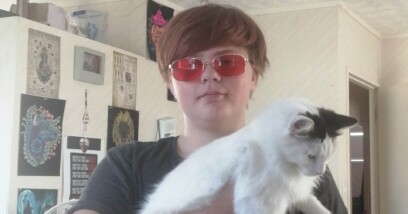 Lucien has swooping brown hair and wears red glasses. In his hands, he holds Wednesday, a mostly-white calico cat.